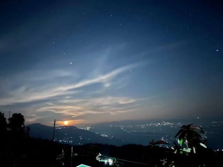 Nightscape view of moon, stars, and twinkling village valley lights from Zambala Dwelling Nest terrace in Darjeeling